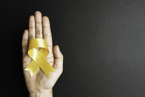 Directly above view of a hand holding yellow suicide prevention awareness ribbon over black background.